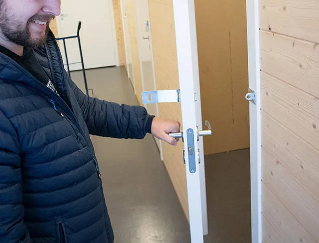 Nærbilde av mann som åpner hvit dør til lagerrom med lyse trekledde vegger.