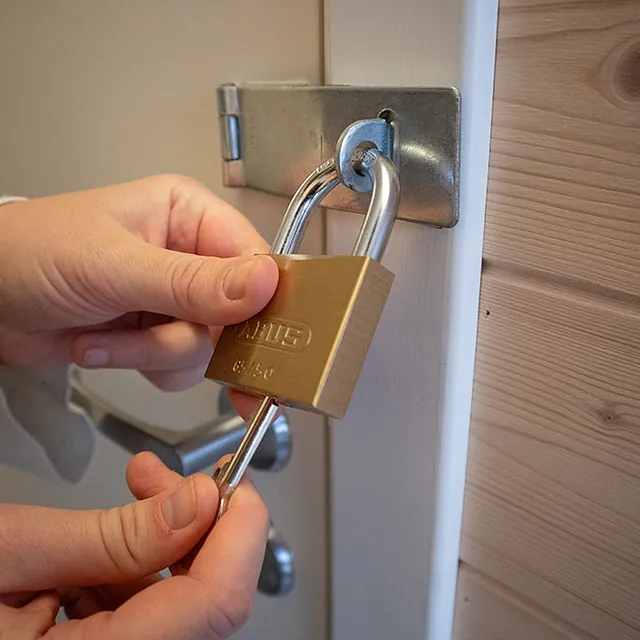 Nærbilde av hender som låser hengelås på hvit dør med trekledning rundt.